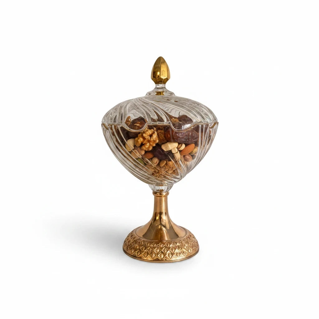 Decorative glass pedestal candy dish with a gold base, filled with nuts and dates.