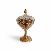 Decorative glass pedestal candy dish with a gold base, filled with nuts and dates.