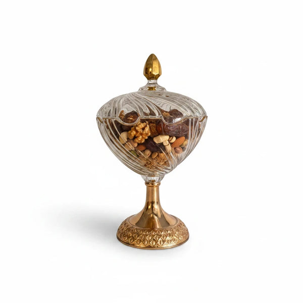 Decorative glass pedestal candy dish with a gold base, filled with nuts and dates.