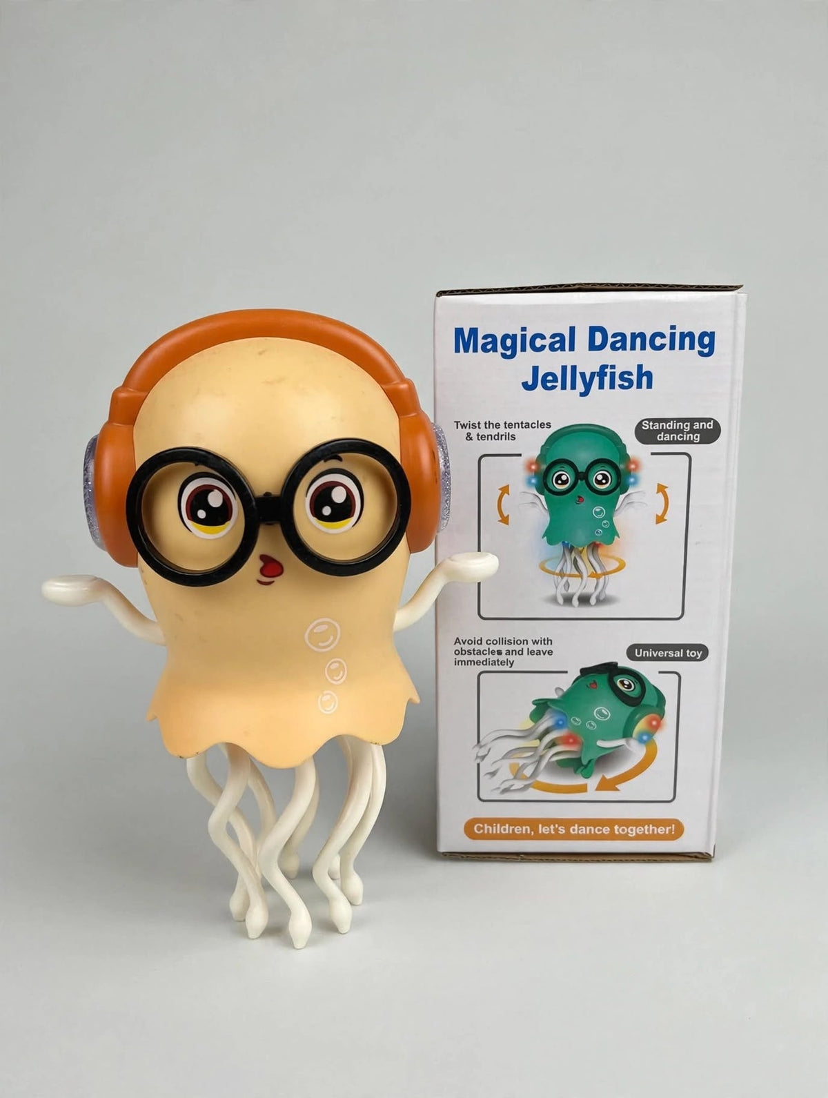 Yellow dancing jellyfish toy with orange headphones and black glasses beside its retail packaging.