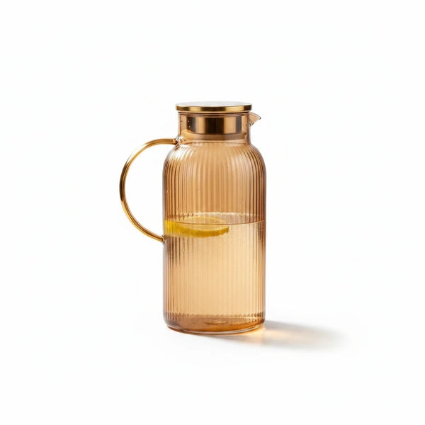 Trendiest amber ribbed glass pitcher with a metallic gold lid and handle, containing water and a lemon slice.