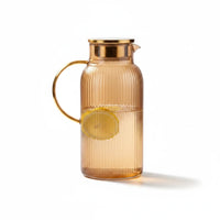 Trendiest amber ribbed glass pitcher with a gold metallic lid and handle, filled with water and lemon slices.