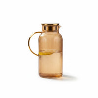 Trendiest amber ribbed glass pitcher with a metallic gold lid and handle, featuring a slice of lemon inside.