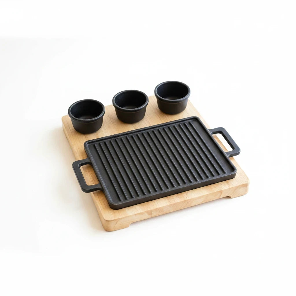 Trendiest cast-iron grill plate with wooden serving board and sauce bowls, close-up product view.