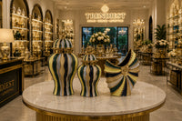 Trendiest hand-finished ceramic urn vases in gold, emerald green, navy, and ivory displayed on a marble table.