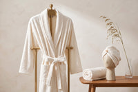 Trendiest spa bathrobe set in cream with matching shower cap and face towel on a wooden stand