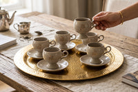 Trendiest cup set with gold floral accents on a large hammered brass tray, held by a hand on a rustic wooden table.