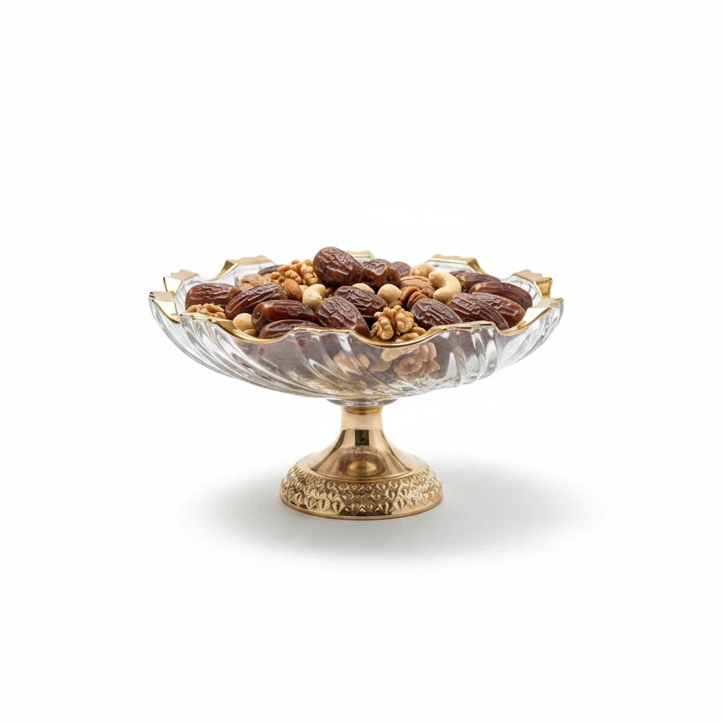 Trendiest decorative glass pedestal bowl with gold rim, filled with assorted nuts and dates on a white background.