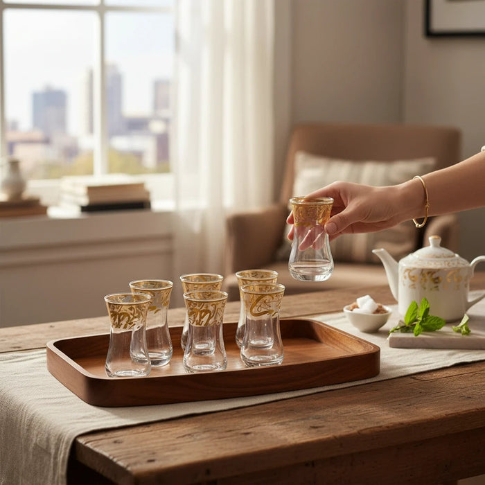 Trendiest set of 6 clear glass tea cups with gold Arabic calligraphy on a wooden tray held by a hand