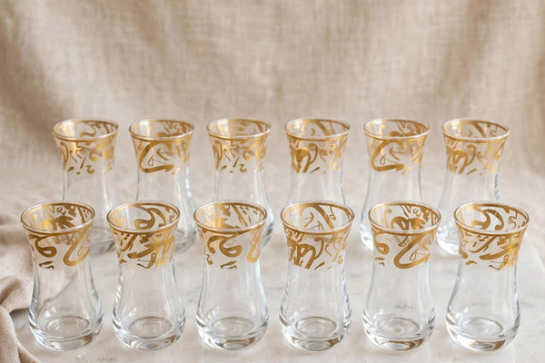 Trendiest set of 6 clear glass tea cups with ornate gold Arabic calligraphy detailing in a tulip-shaped silhouette.