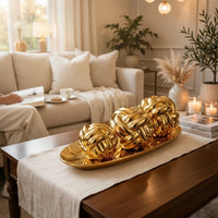 Trendiest decorative gold knot sculpture set with three spheres on an oval tray displayed on a wooden coffee table.