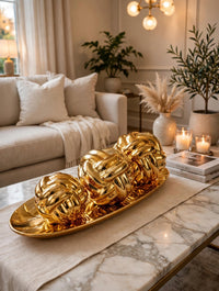 Trendiest decorative gold knot sculpture set with three spheres on an oval tray displayed on a marble coffee table.