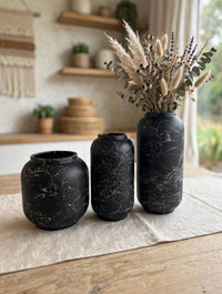 Trendiest set of three matte black ceramic vases with white marble veining, styled with dried florals on a table.