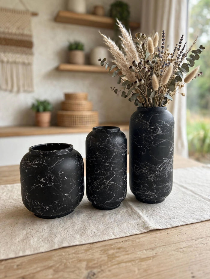 Trendiest set of three matte black ceramic vases with white marble veining, styled with dried florals on a table.