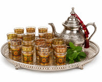 Trendiest set of 12 Moroccan tea glasses with gold geometric patterns and matching silver teapot on a serving tray.
