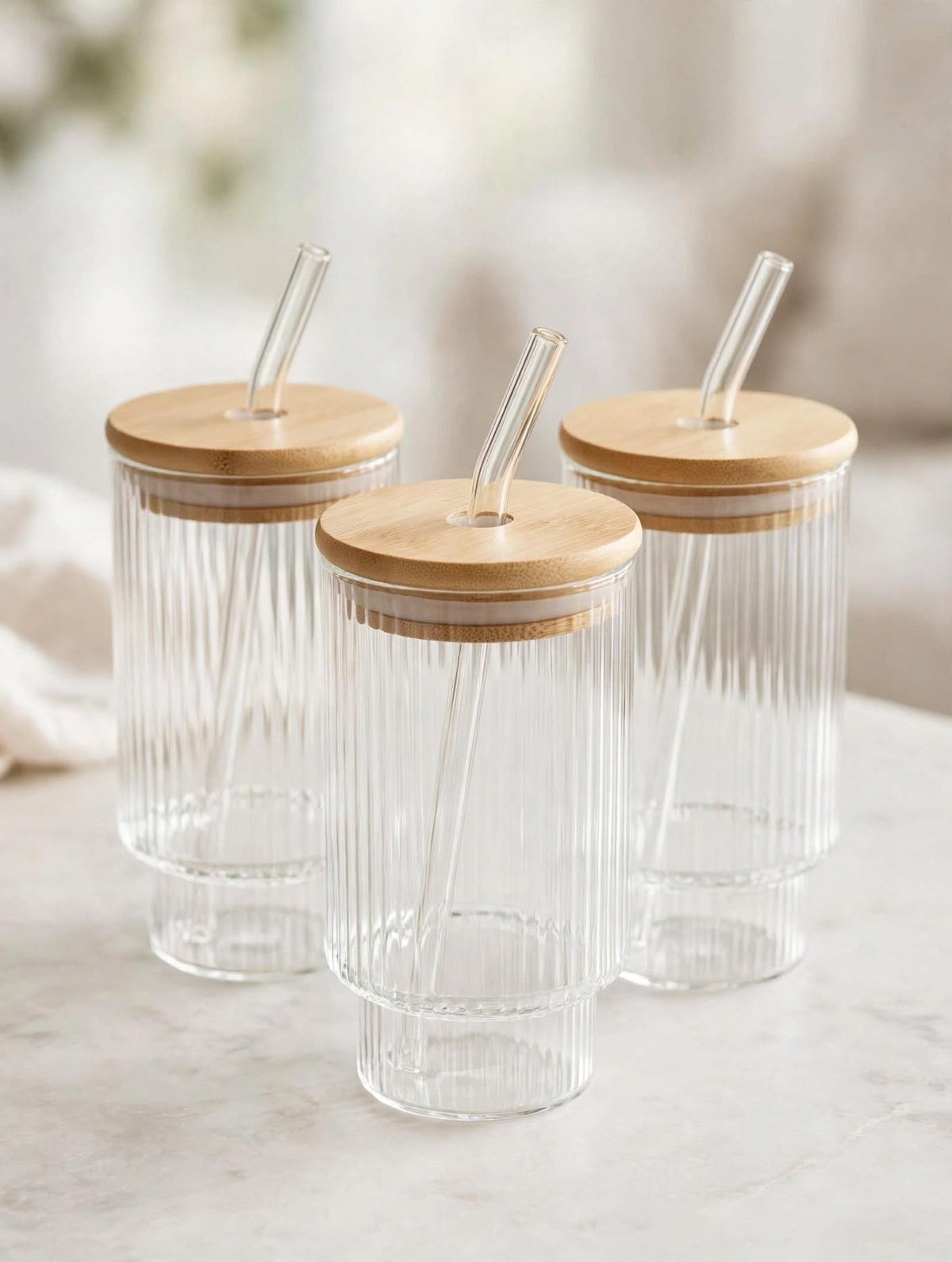Trendiest ribbed glass tumbler set with bamboo lids and reusable glass straws on a marble surface