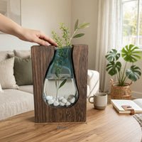 Trendiest handcrafted dark wood vase with a blue-tinted glass insert holding a green sprig and white pebbles