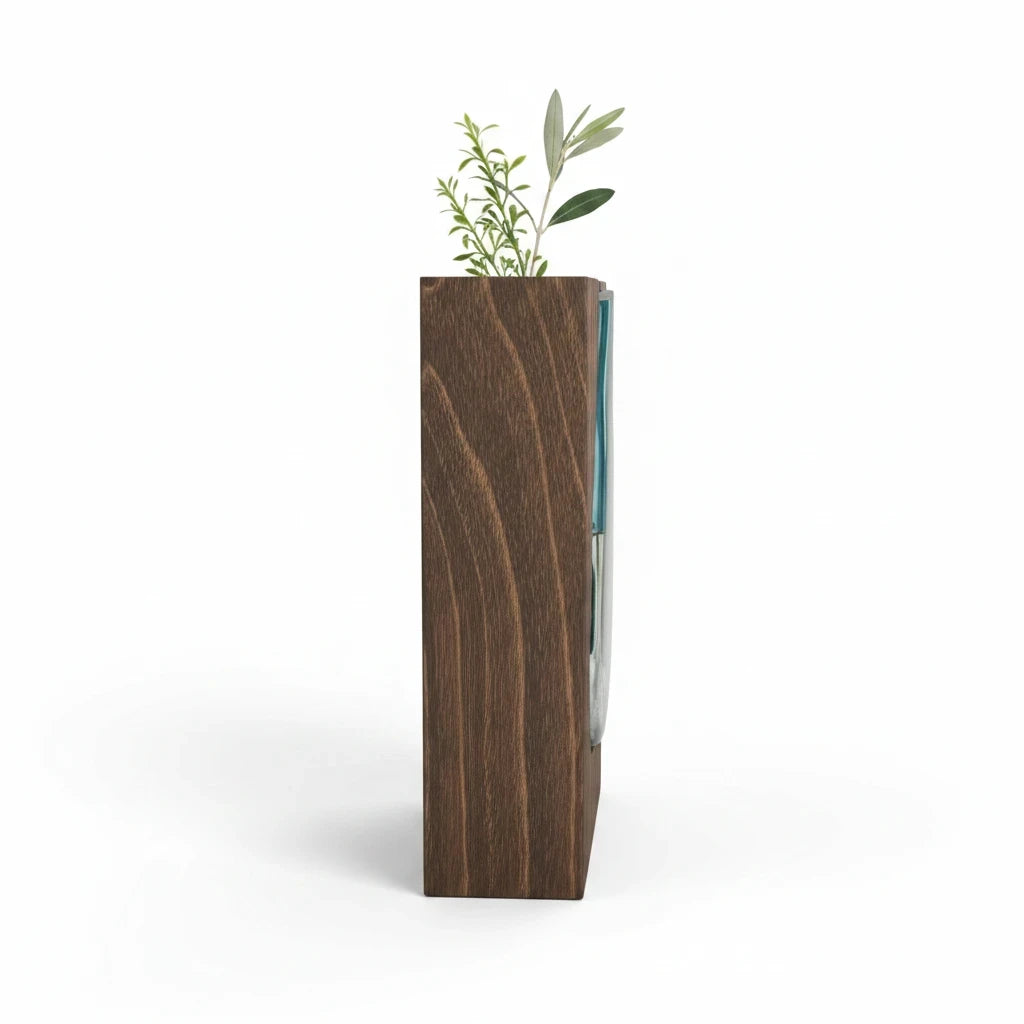 Trendiest handcrafted dark wood vase with a blue-tinted glass insert holding a green botanical stem, side view.