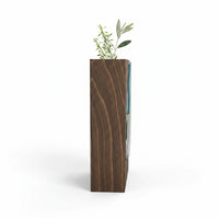 Trendiest handcrafted dark wood vase with a blue-tinted glass insert holding a green botanical stem, side view.